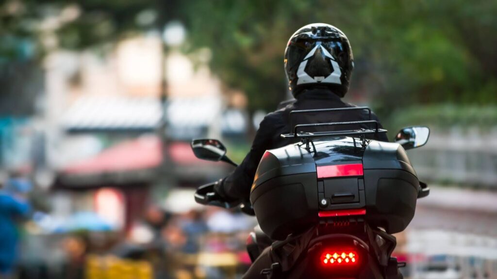 Back view of a courier on a motorcycle with suitcase on the back on a blurred street