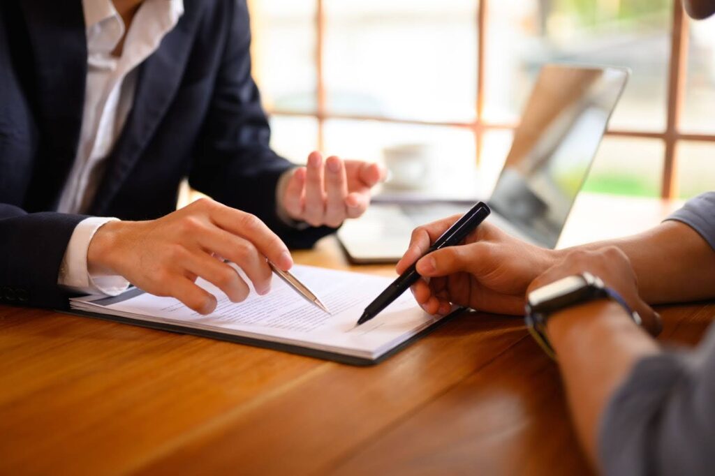 Closeup of insurance agent pointing at contract showing male client where to sign