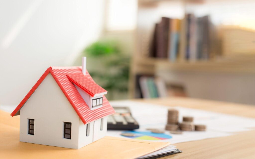 Small model home on a table next to a calculator, printed graph, and pile of coins to represent home insuance