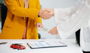 Insurance agent shaking hands and exchanging money with customer behind table with toy cars to represent Georgia dealer insuarnce