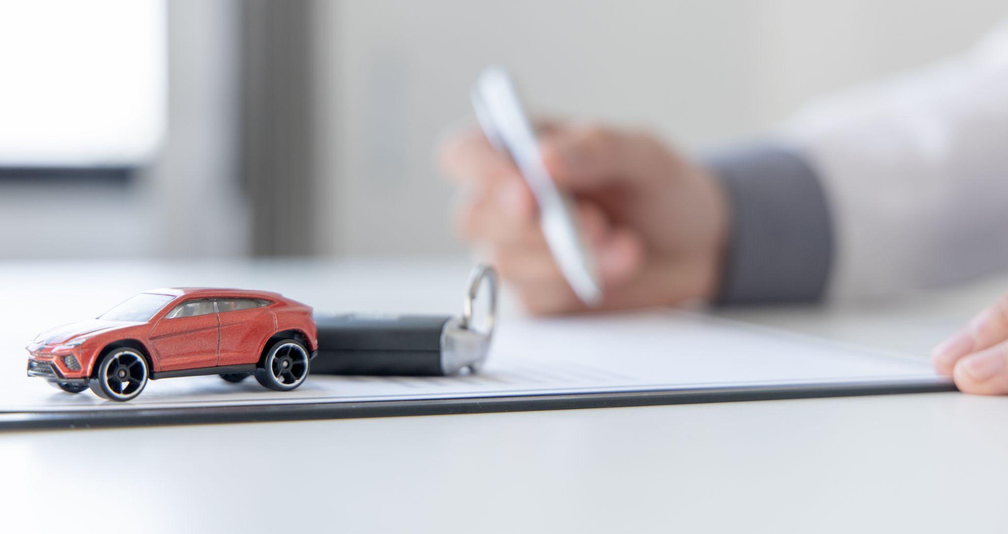 Man signing a document with a toy car and keys on the table to represent Missouri auto dealer insurance